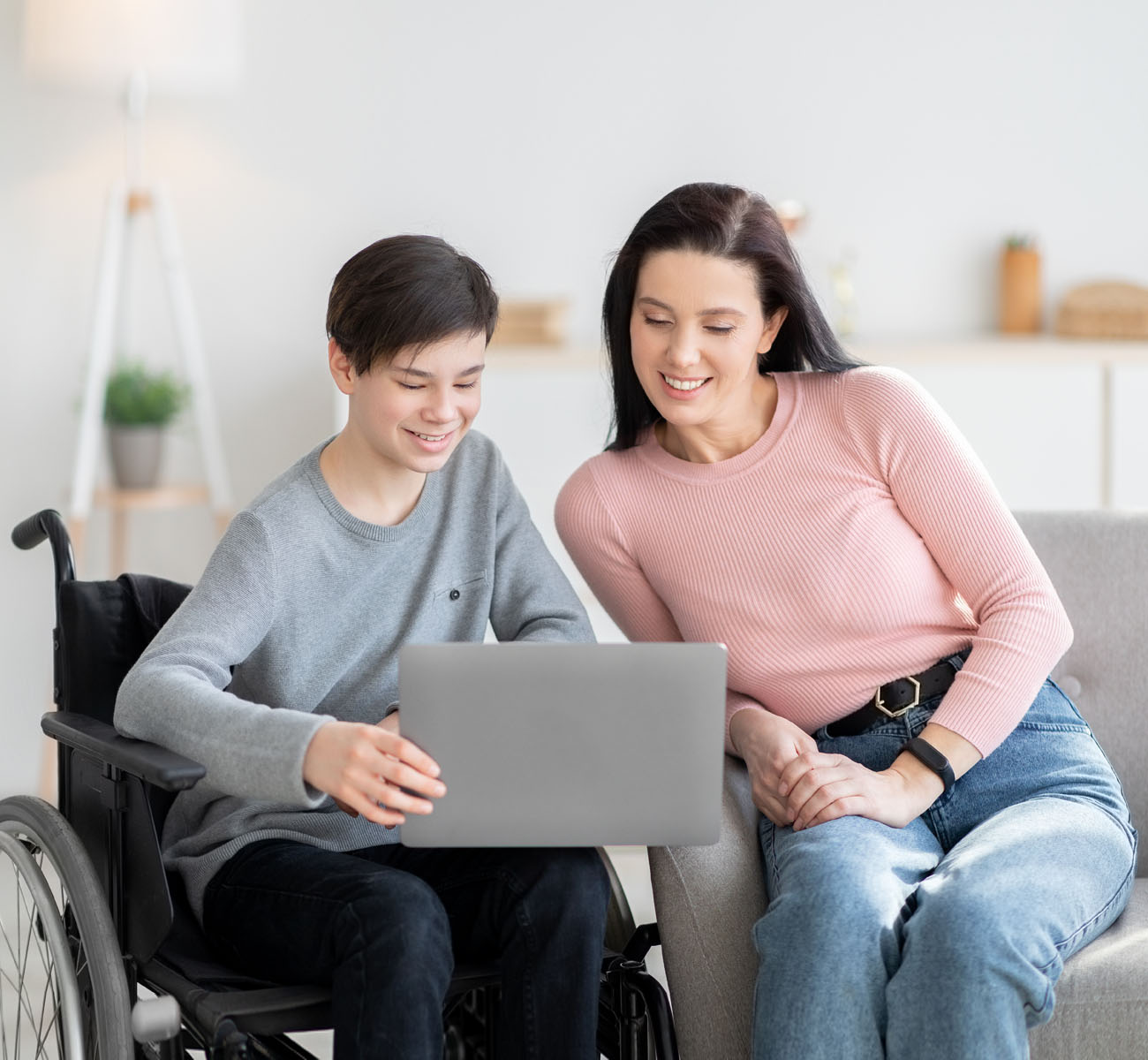 Home schooling. Handicapped teen boy in wheelchair learning online together with his mother indoors